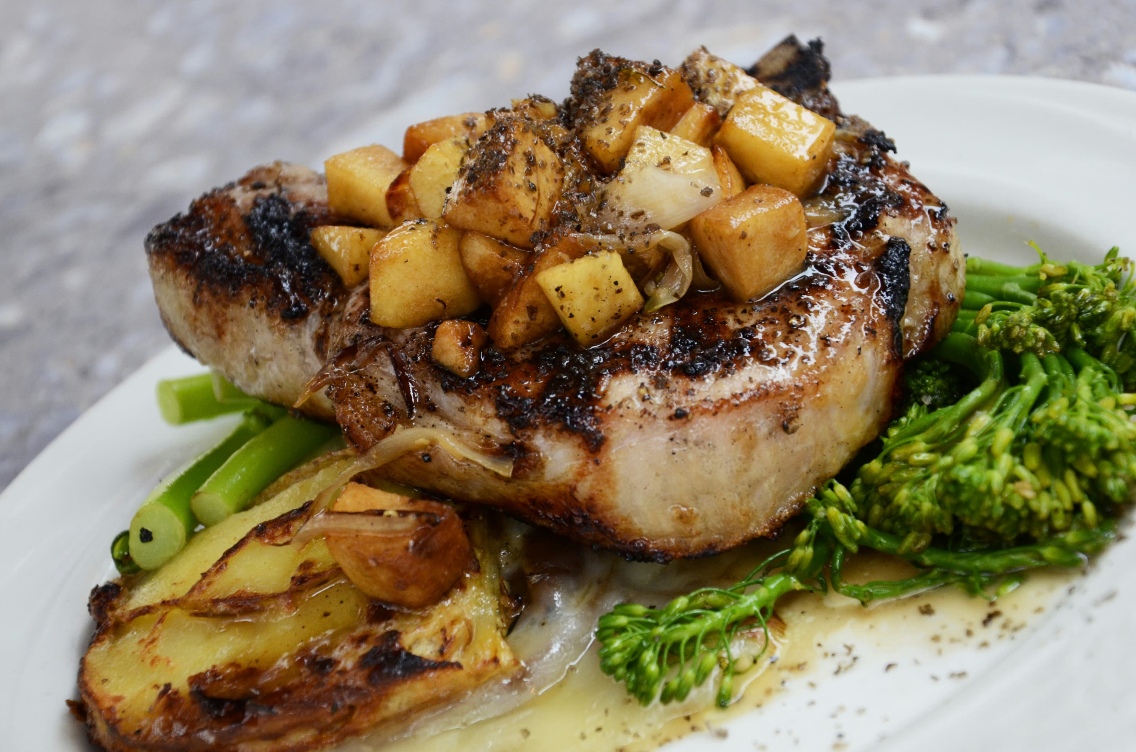 A grilled pork chop with roast potatoes and greens